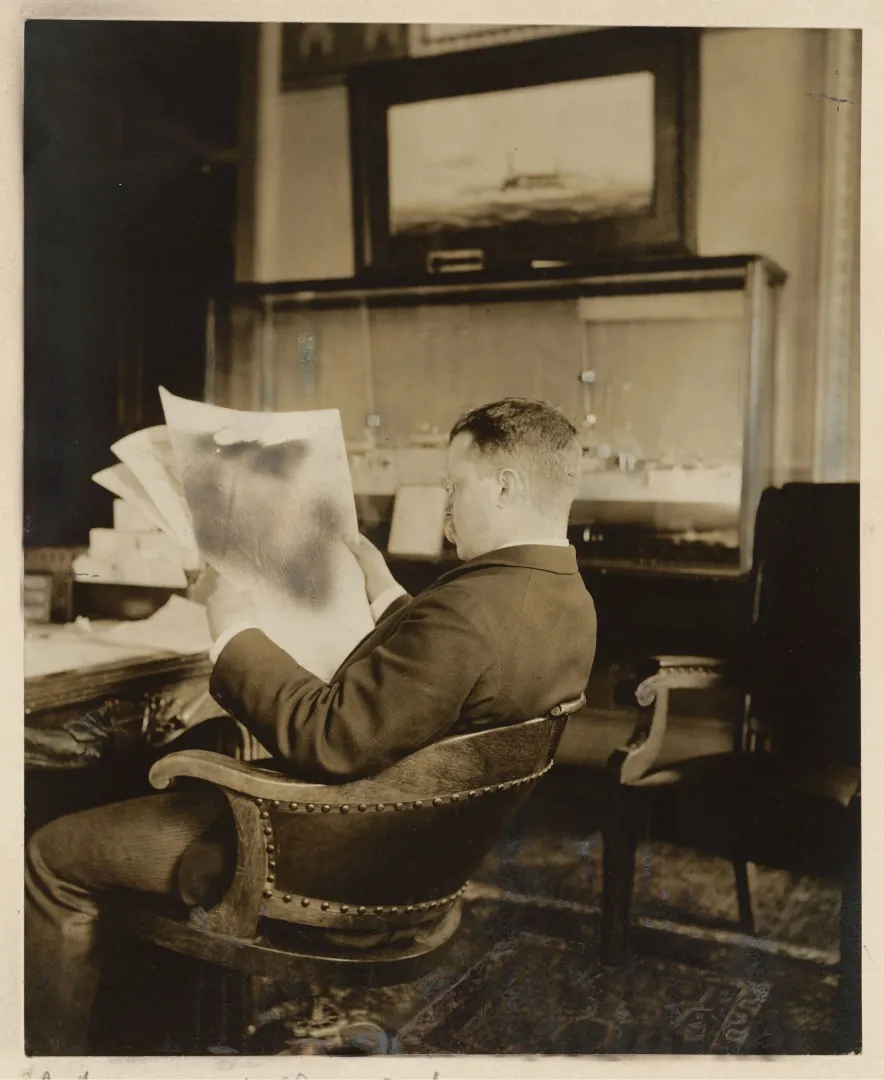 Theodore Roosevelt seated in a chair reading a newspaper