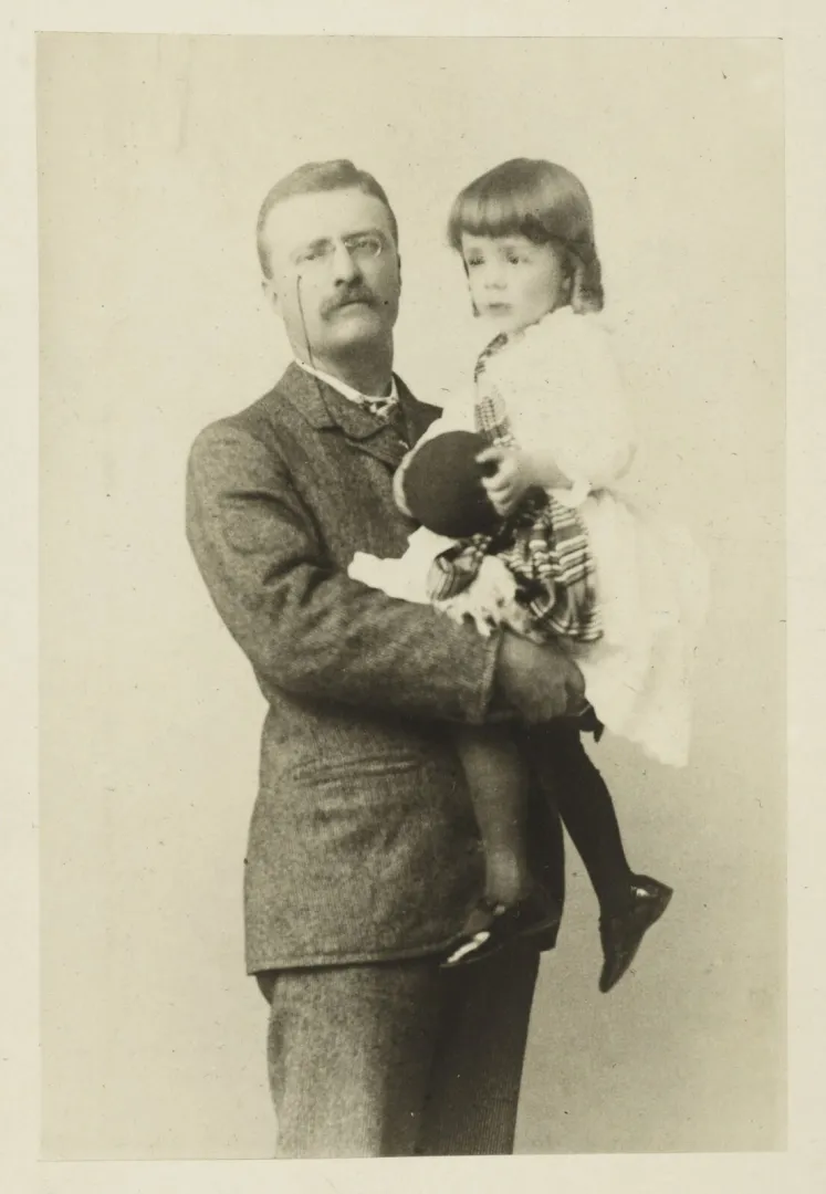 Theodore Roosevelt in a tweed suit standing and holding his young son Ted in his arms