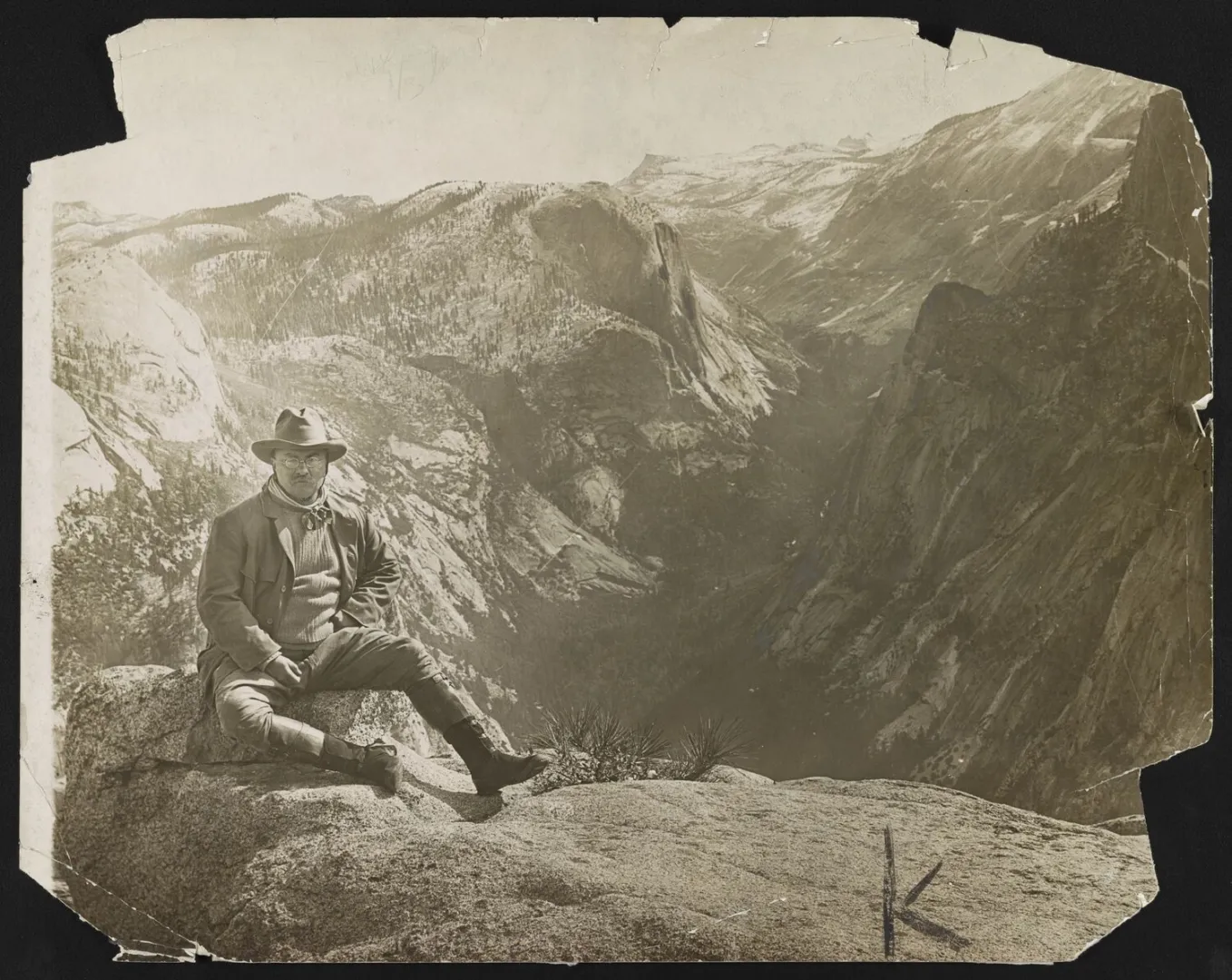 Theodore Roosevelt seated on a rock amid dramatic canyon wilderness scenery