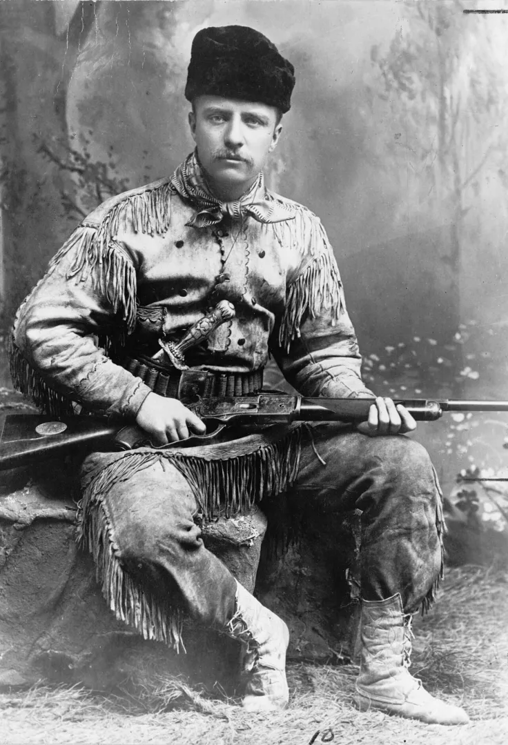 Studio portrait of Theodore Roosevelt in a fringed buckskin hunting suit holding a rifle