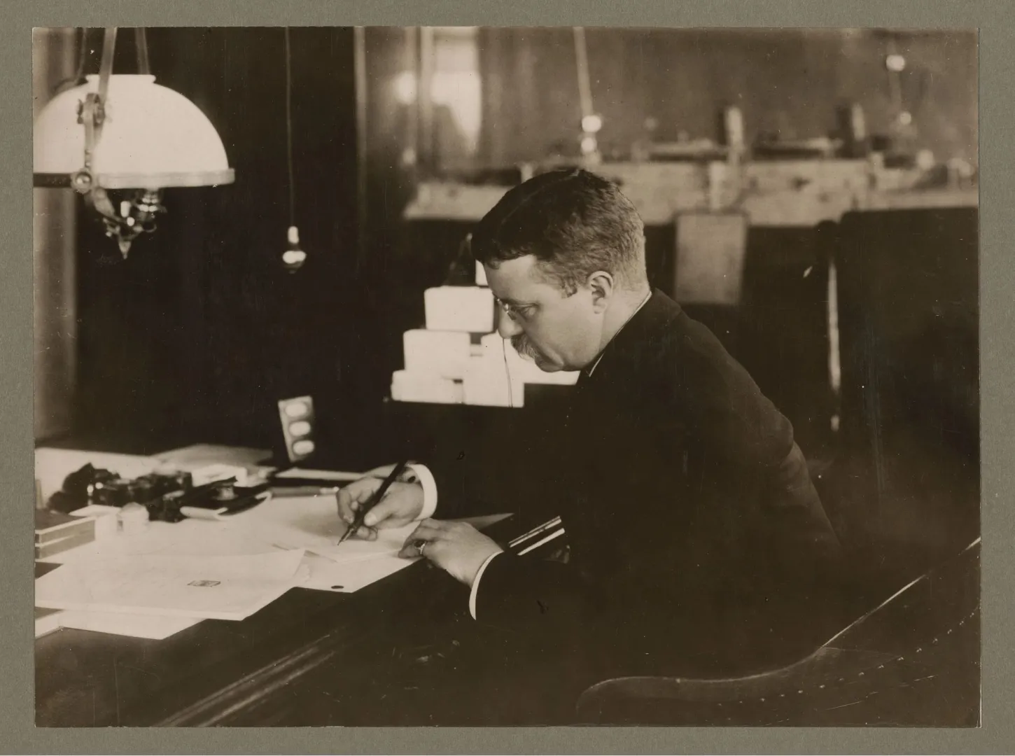 Theodore Roosevelt writing at his desk beneath a lamp