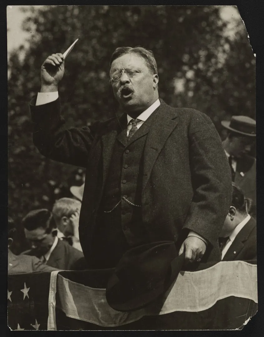 Theodore Roosevelt speaking forcefully from a flag-draped outdoor platform