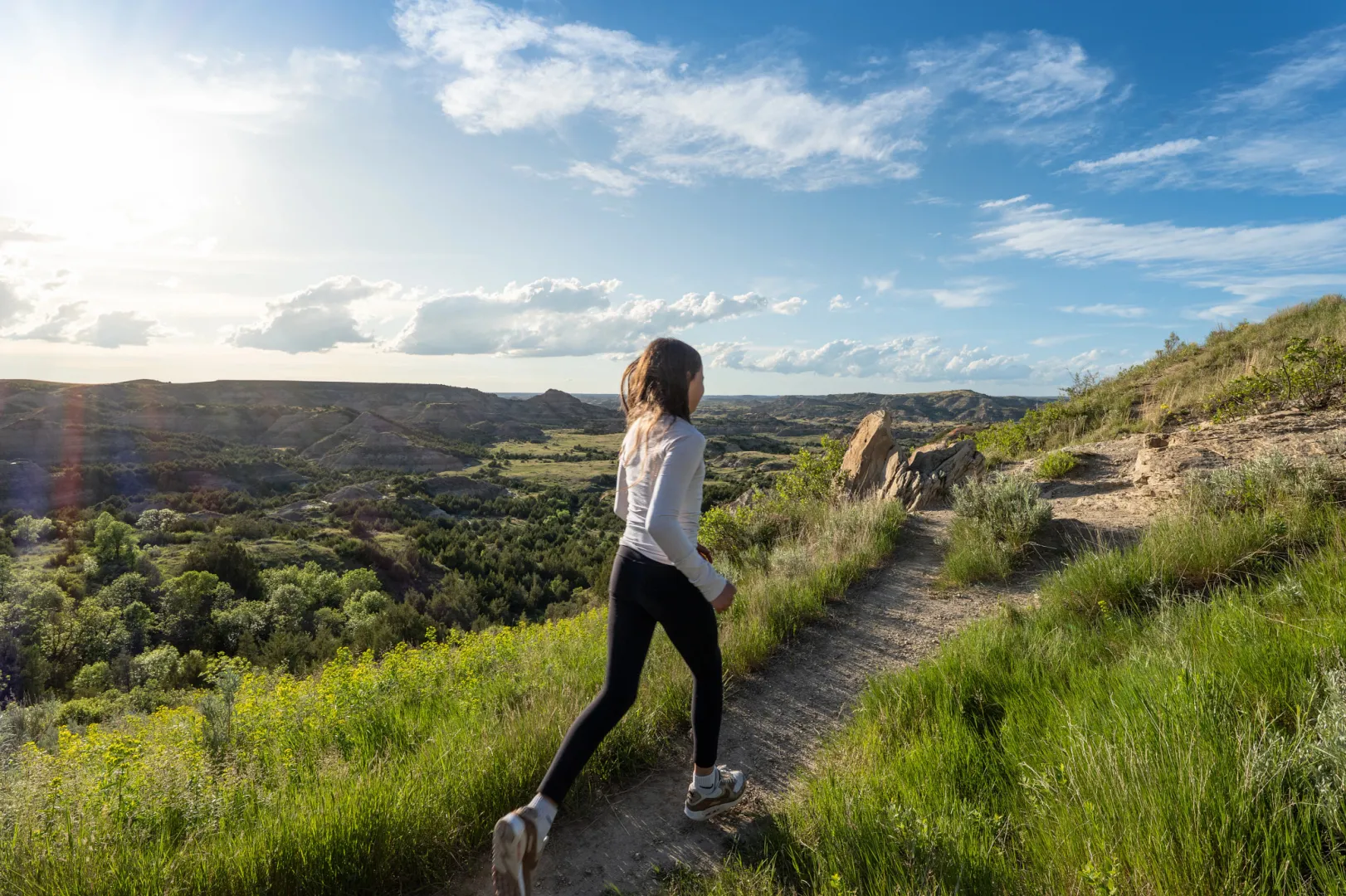 A visitor walking a grassy trail along the rim above the badlands in Theodore Roosevelt National Park