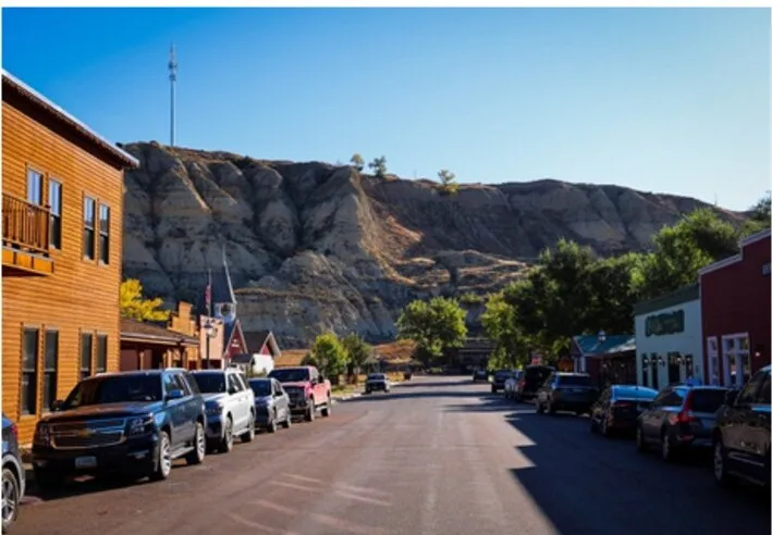 Cars parked along the main street of downtown Medora, North Dakota, with striped badlands bluffs rising behind the storefronts
