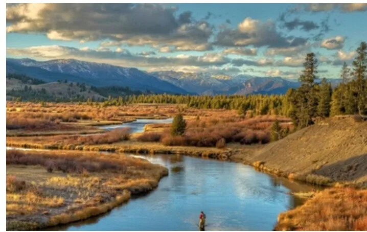 The Yellowstone River winding through open valley below snow-capped mountains near West Yellowstone, Montana