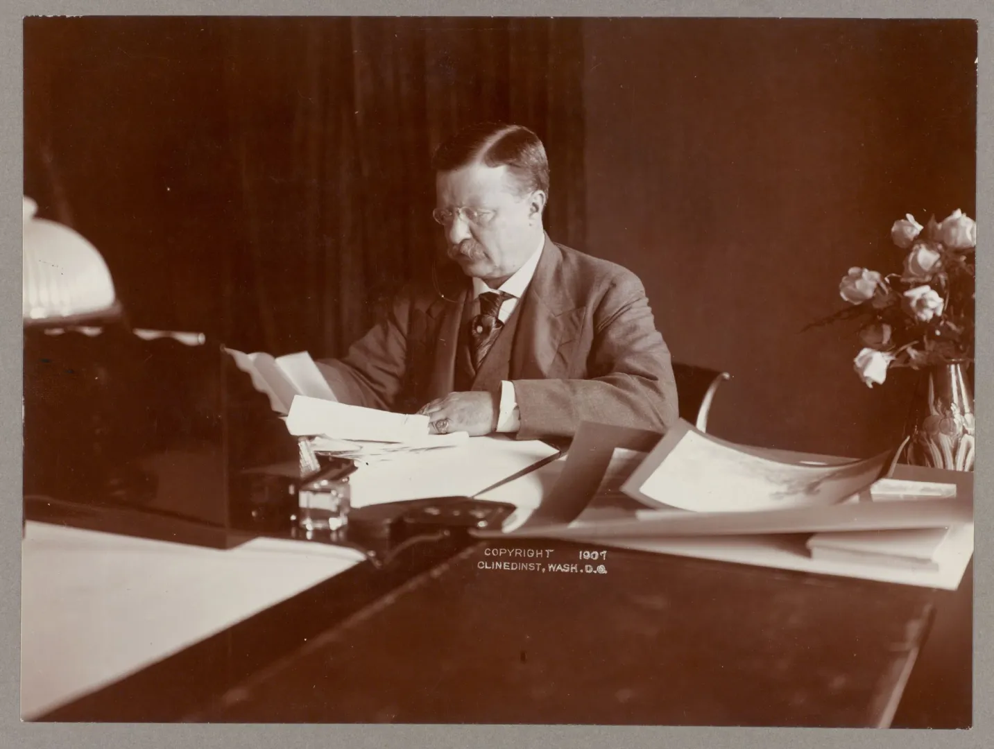 President Theodore Roosevelt seated at his desk reviewing papers