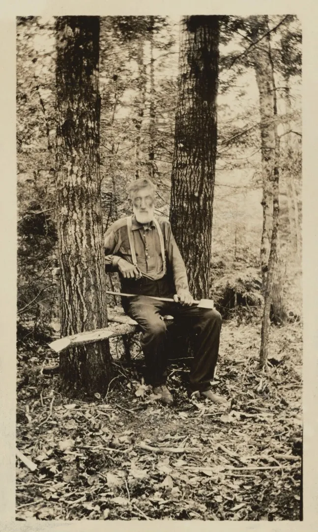 Bill Sewall seated in the Maine woods with a rifle