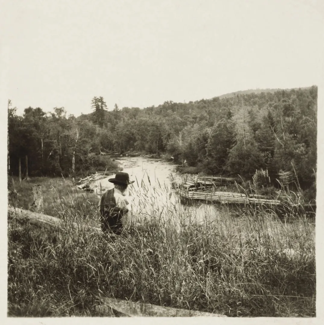 A figure resting beside a river in the Maine north woods