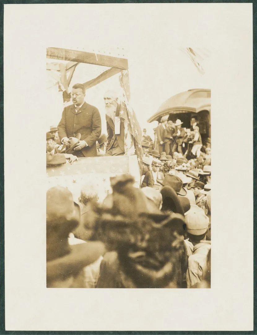 Theodore Roosevelt speaking to a crowd from a flag-draped platform