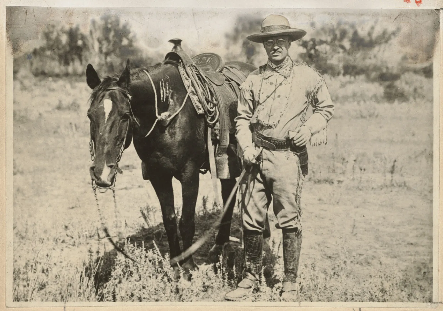 Theodore Roosevelt standing beside his horse on the open range during a cattle round-up in 1885.
