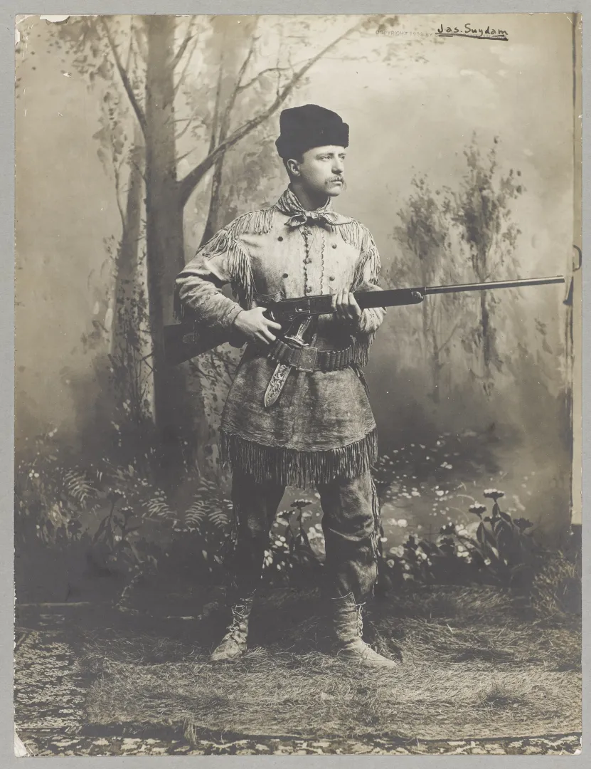 Theodore Roosevelt in a fringed buckskin hunting suit holding a rifle, 1885 studio portrait.