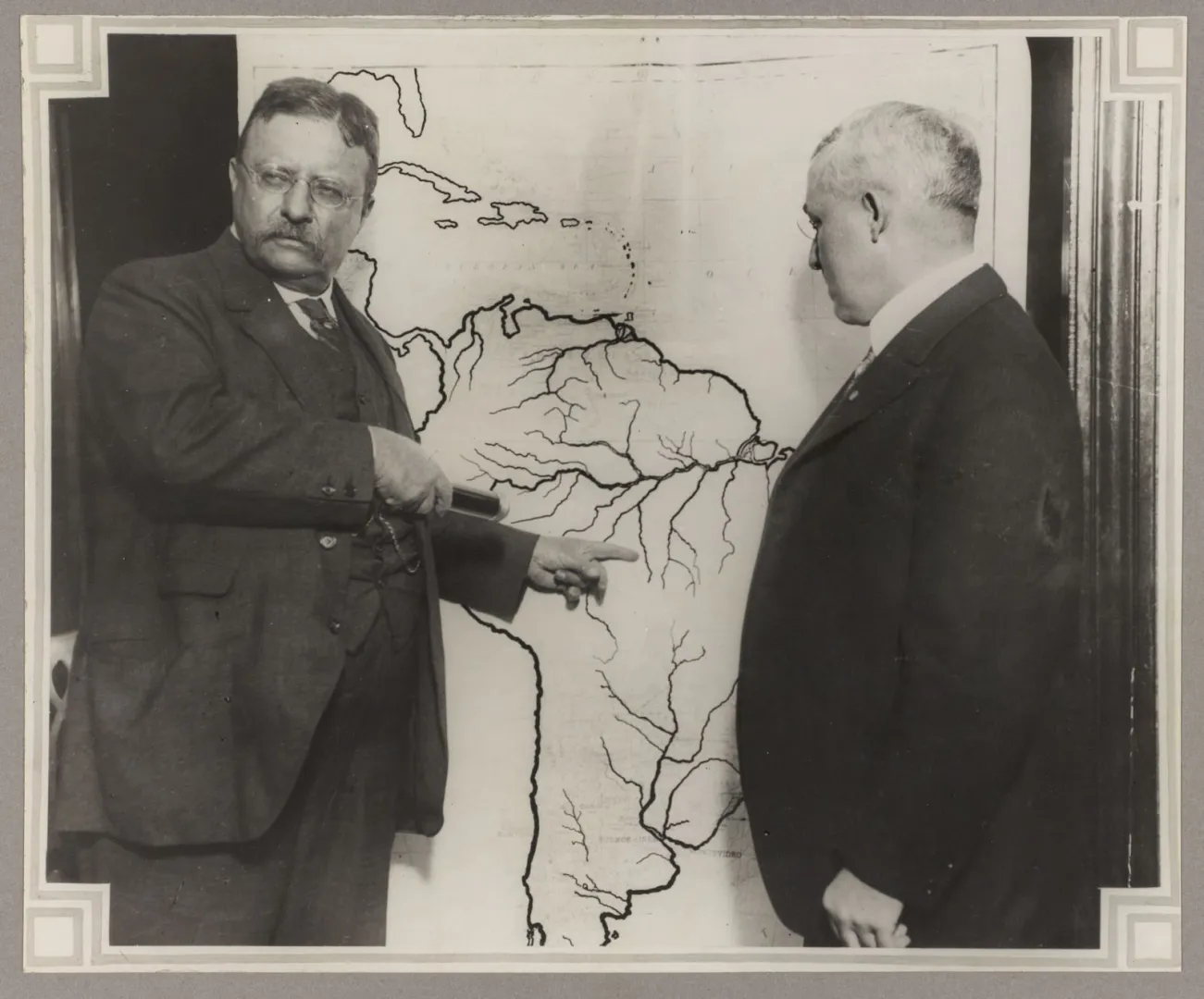 Theodore Roosevelt pointing to a map of South America showing the area explored on the Roosevelt-Rondon Expedition, 1913