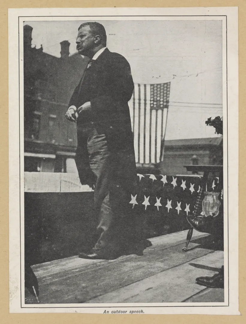 Theodore Roosevelt speaking from a bunting-draped platform before an American flag