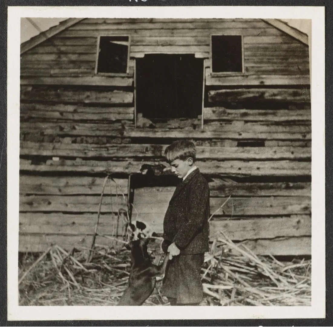 Archie Roosevelt with his dog Skip beside the weathered wall of the Pine Knot cabin