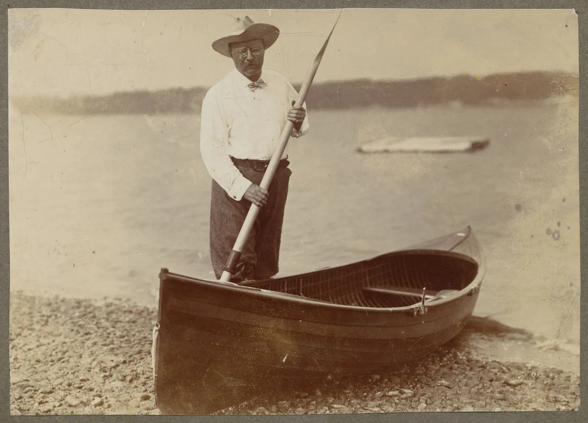 Theodore Roosevelt standing and poling a boat on the water at Oyster Bay