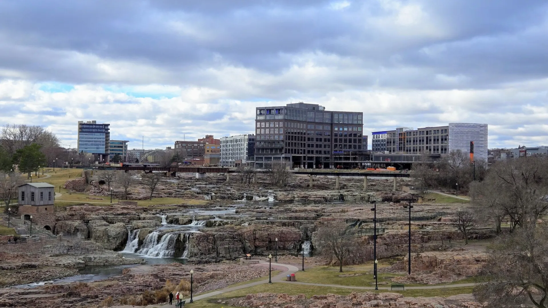 The Big Sioux River dropping over pink quartzite at Falls Park with downtown Sioux Falls behind