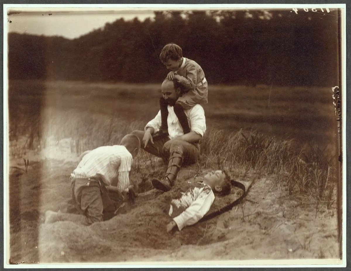 Quentin Roosevelt perched on a man’s shoulders while Archie plays in the sand at Sagamore Hill, 1904