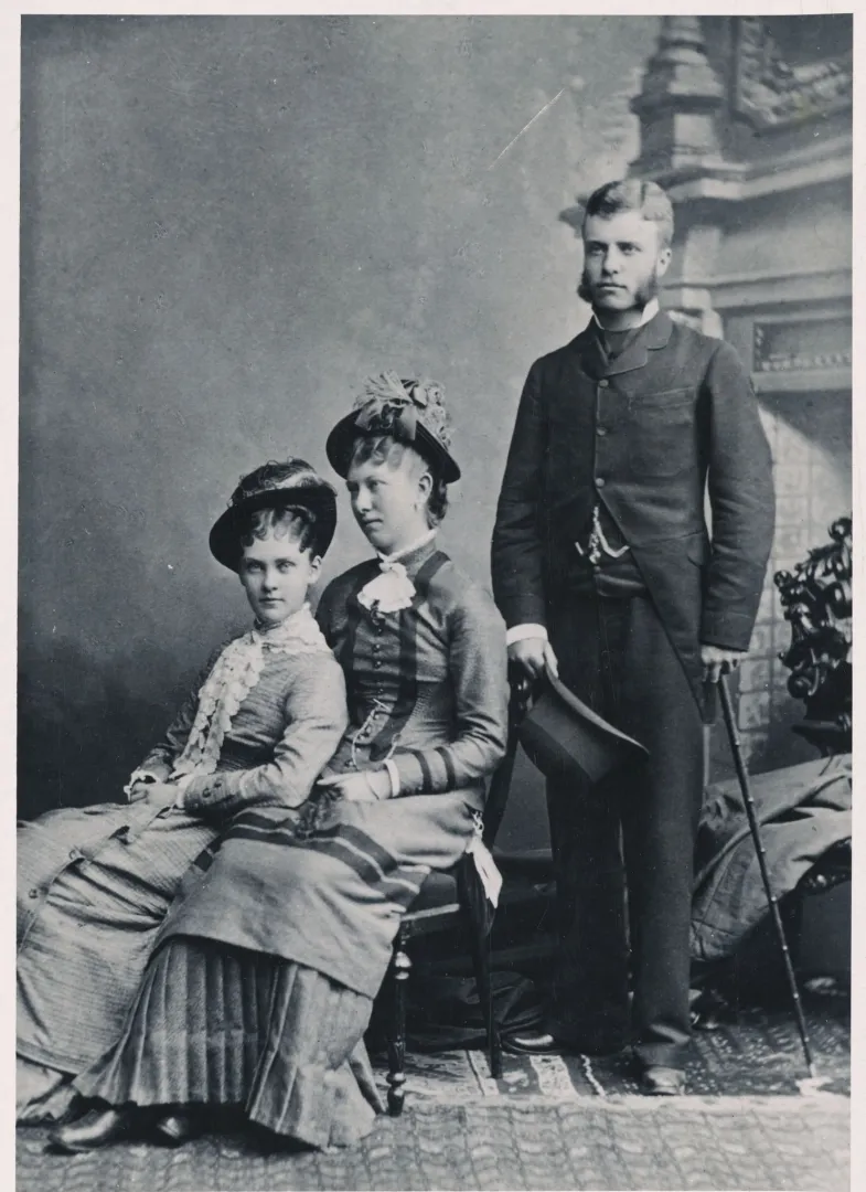Two seated young women and a standing young man in a studio portrait
