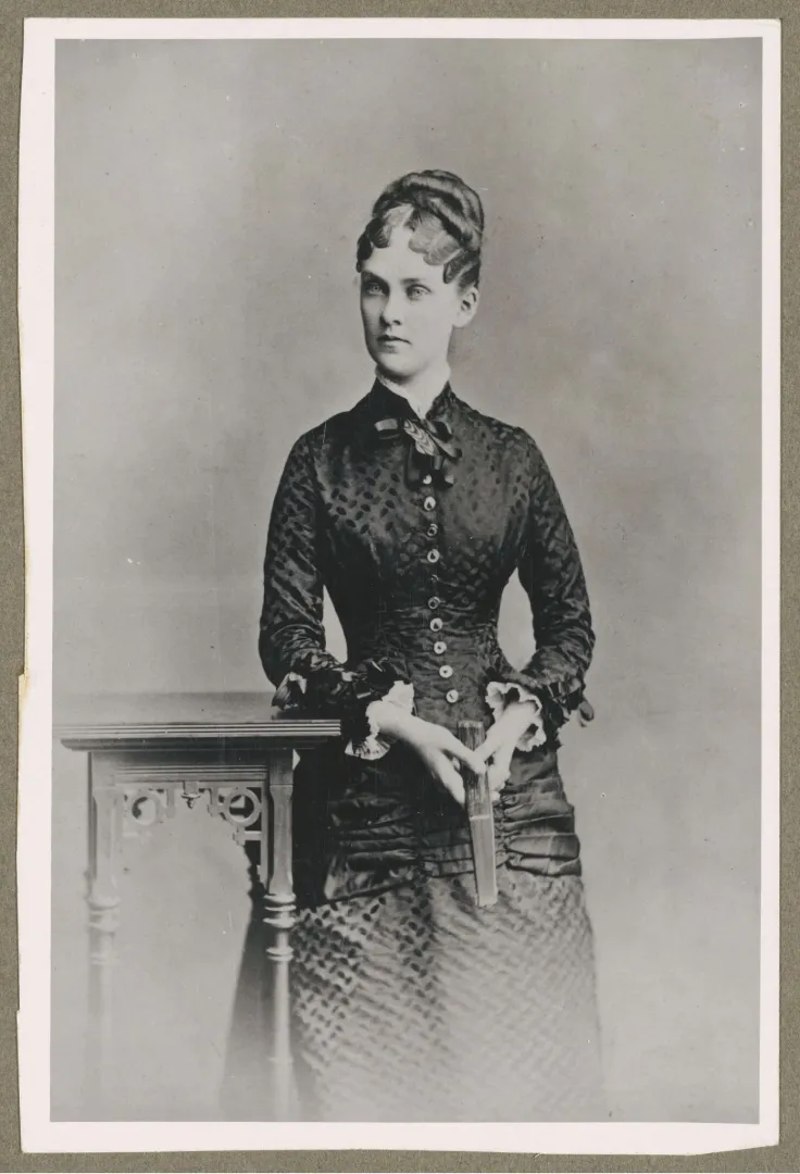 Young woman in a dark buttoned dress standing beside a small table