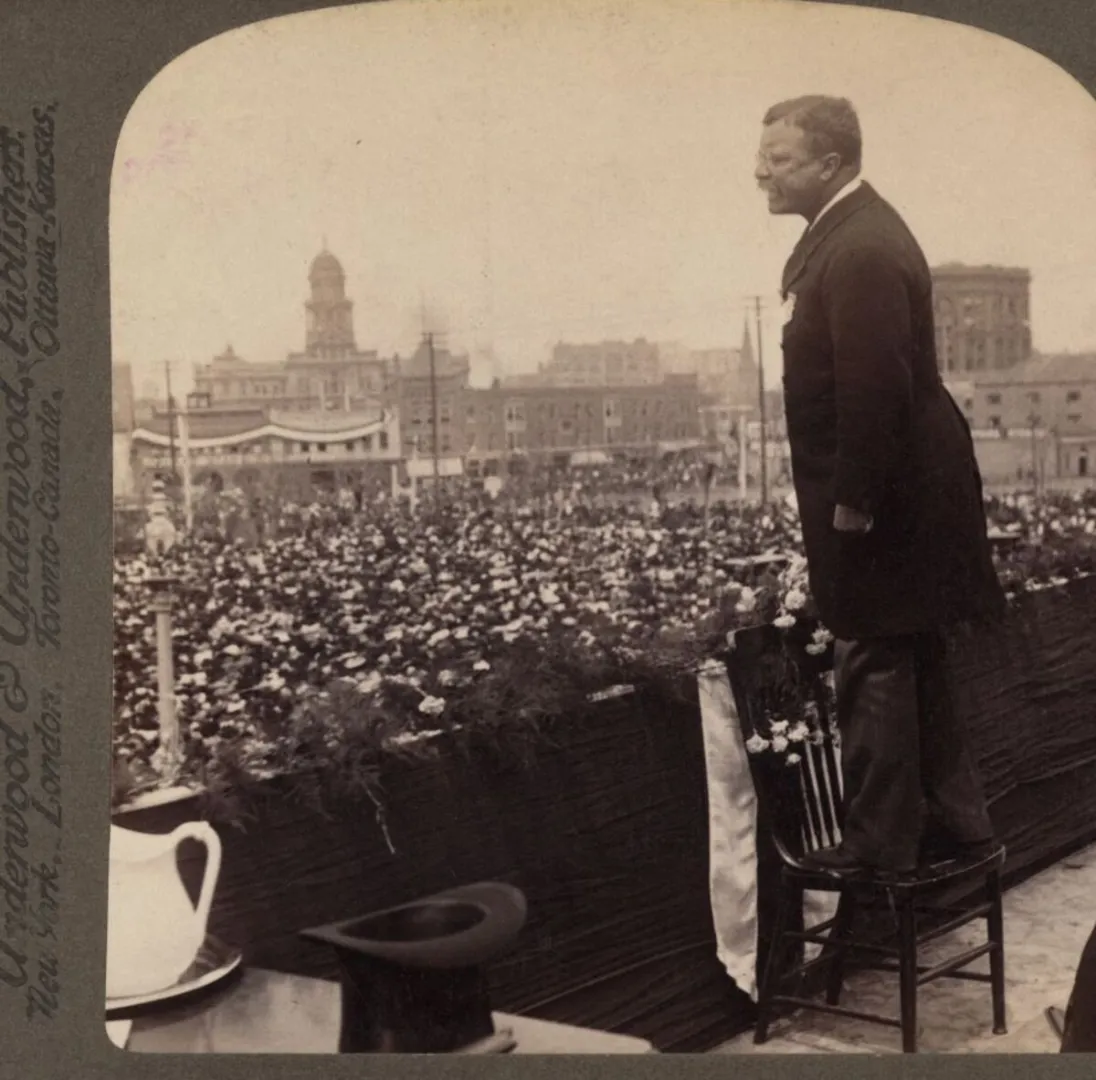 Theodore Roosevelt standing on a draped platform addressing a large crowd, 1905