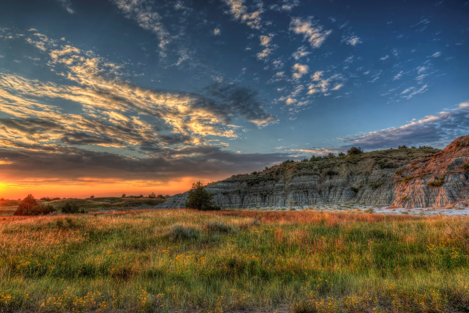 Vivid sunset over the Badlands with red scoria hills and prairie in the foreground