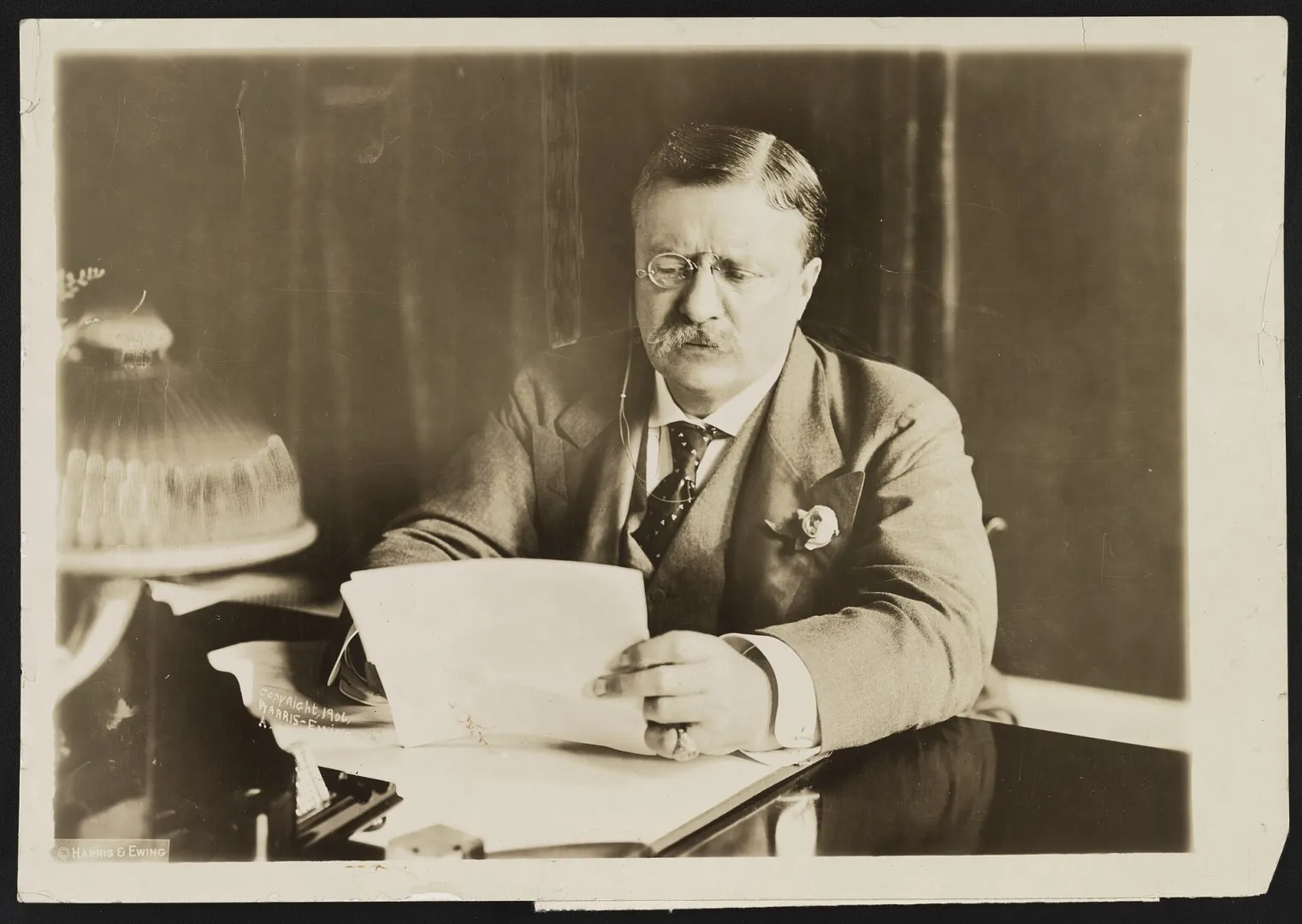 Theodore Roosevelt seated at a desk reading a document