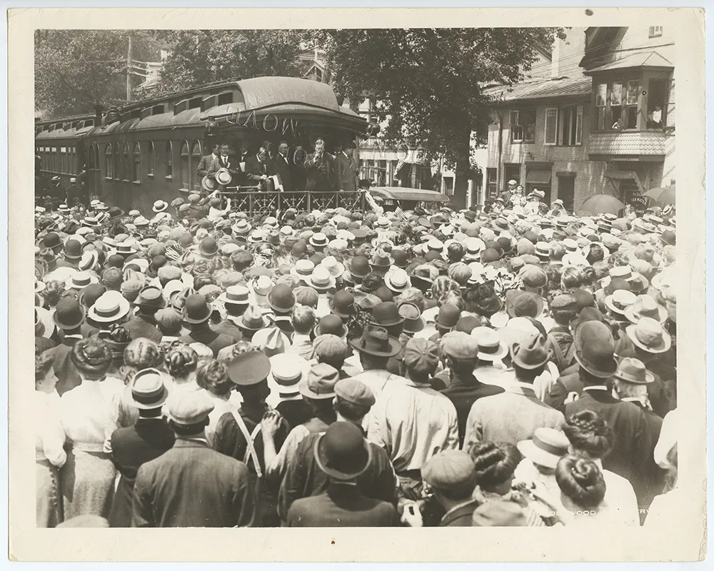 Theodore Roosevelt delivering a speech from the rear platform of a train to a large crowd in 1912