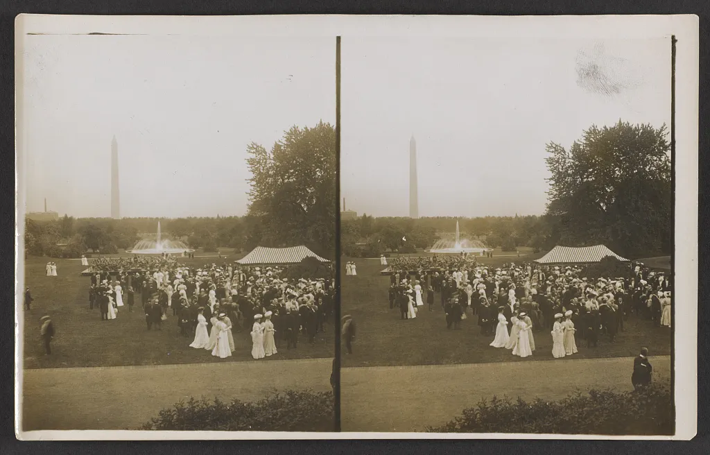 Stereograph of a crowd in summer dresses and hats on a wide lawn, with a striped tent, a fountain and the Washington Monument behind.