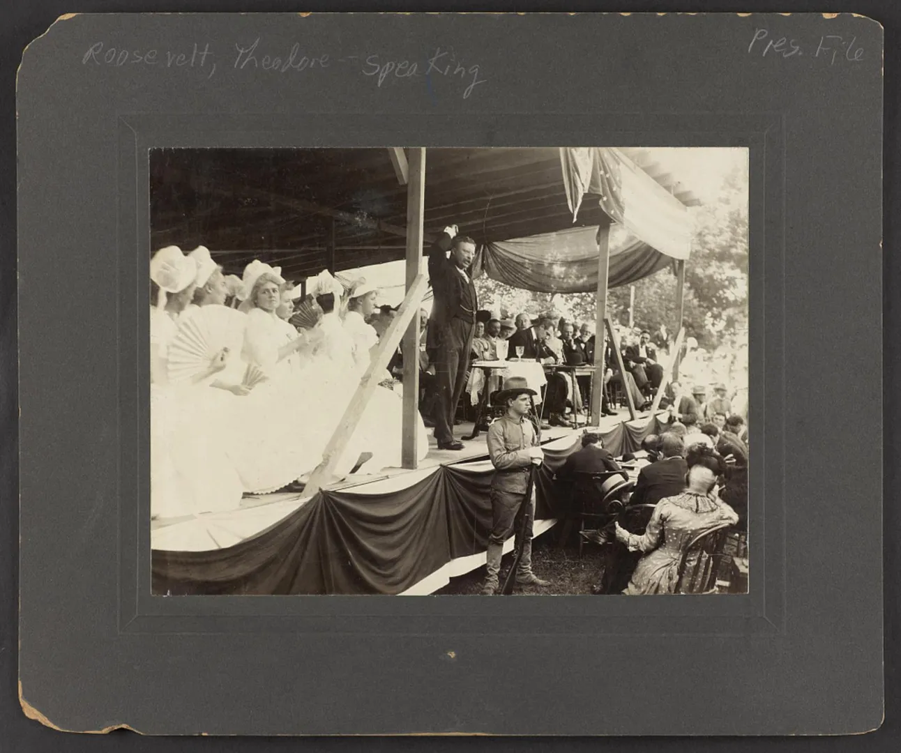 Theodore Roosevelt speaking to a seated audience from a flag-draped platform, 1903