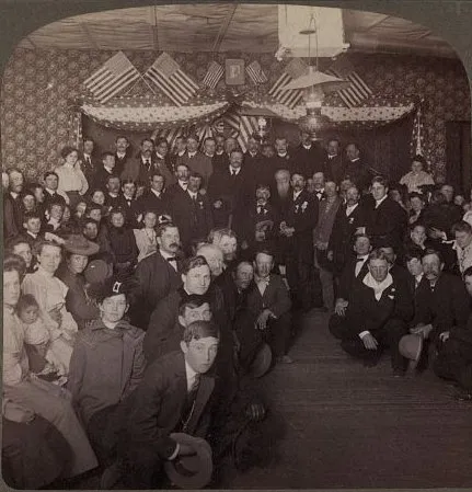 A large crowd of men, women, and children posed in a hall decorated with flags and bunting.