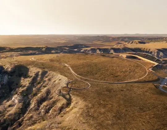 Aerial view of a vast, sunlit landscape with winding dirt paths and hills.