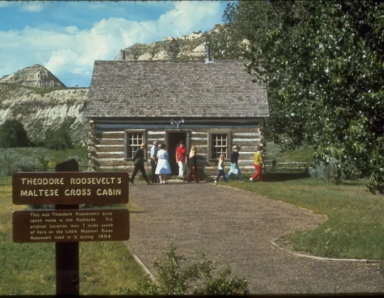 Vintage photo of people visiting the Maltese Cross Cabin beside its sign