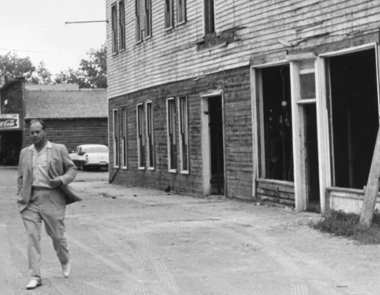 Harold Schafer walking past old buildings in Medora, black and white