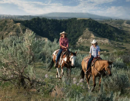 Two riders in sagebrush with buttes behind