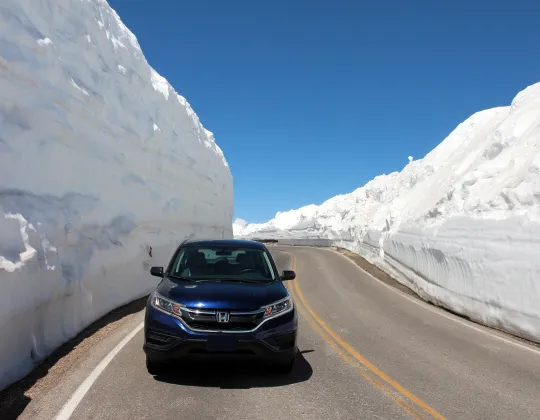 A car driving between high walls of plowed snow on the Beartooth Highway