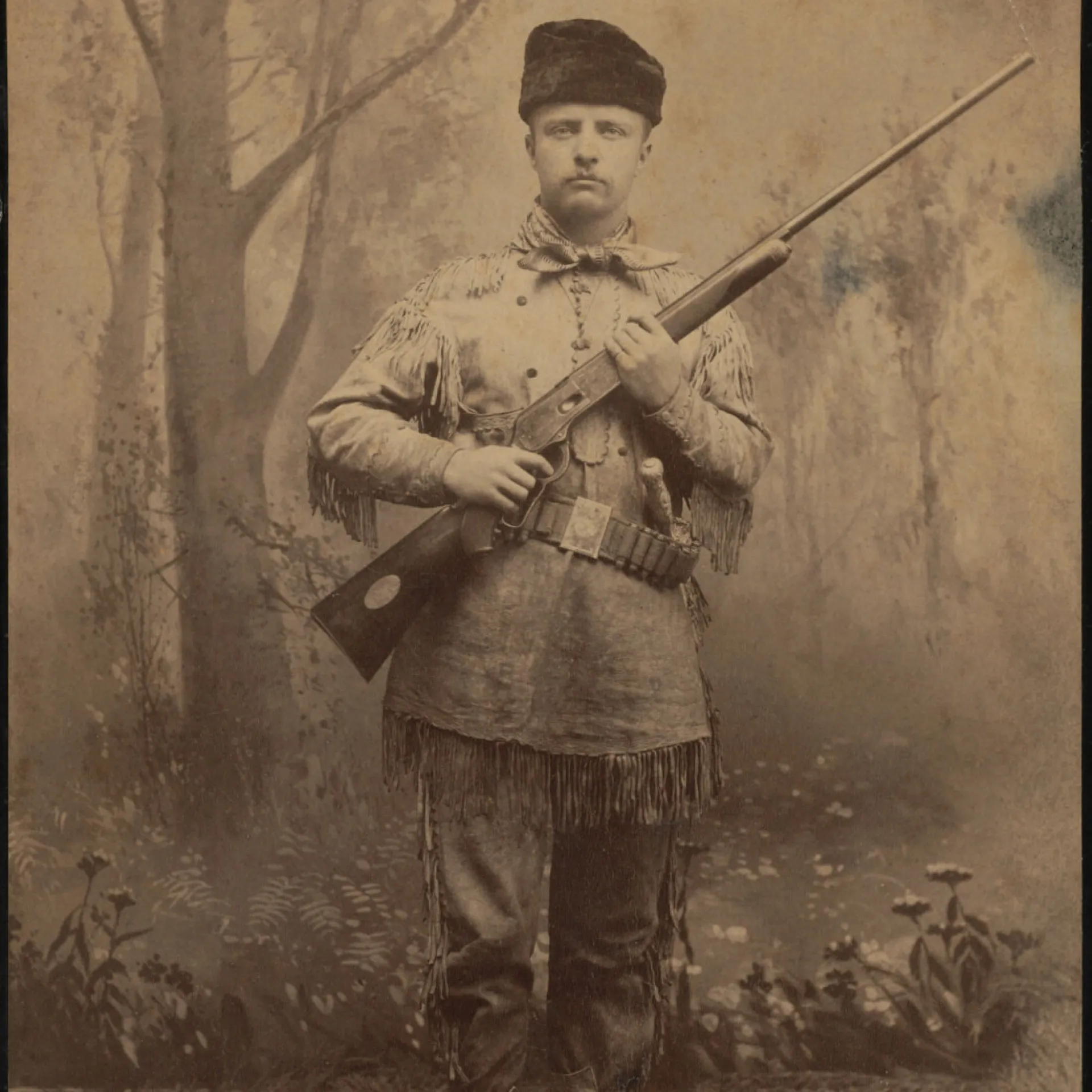 Young Theodore Roosevelt in a fringed buckskin hunting suit holding a rifle, 1880s studio portrait