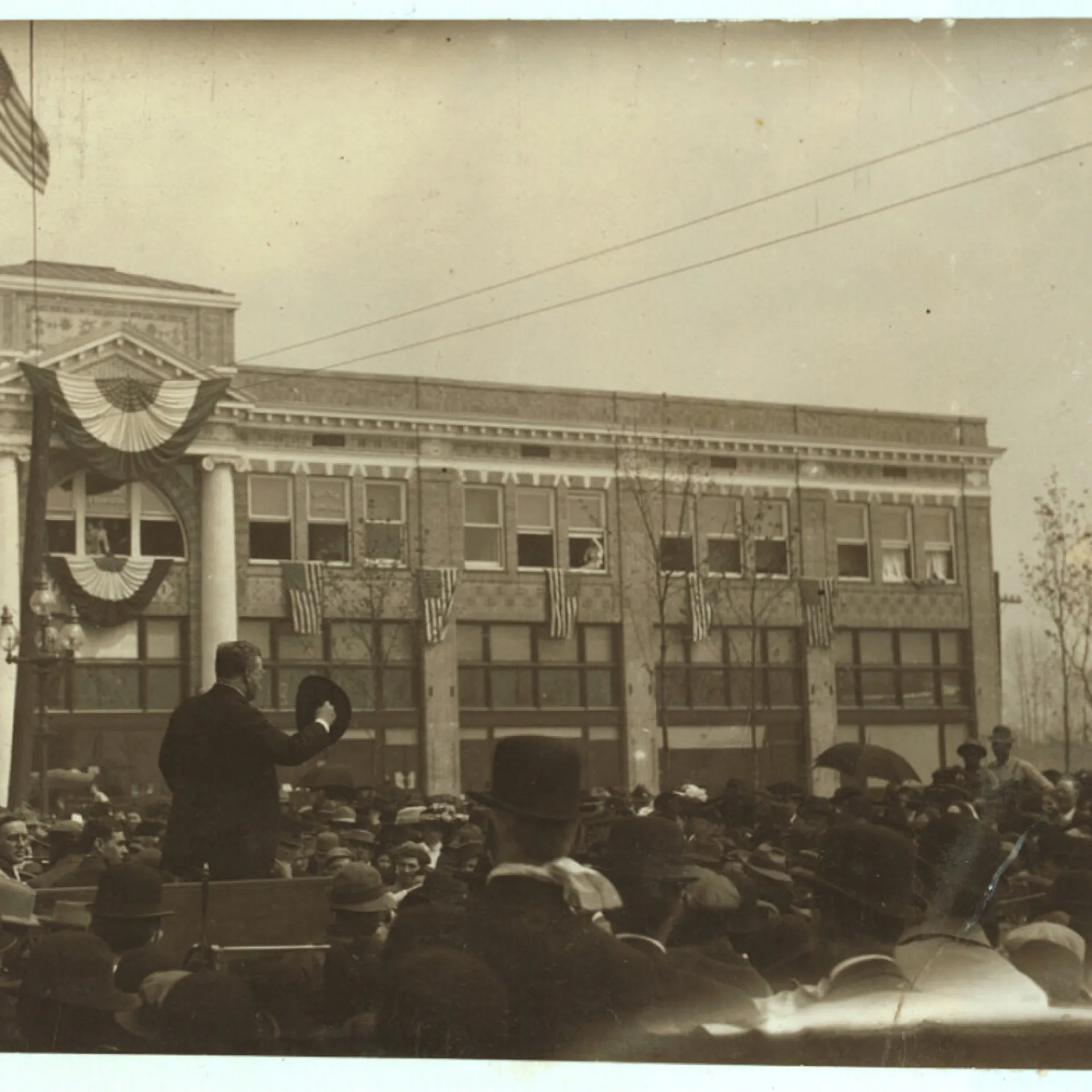 Theodore Roosevelt addressing a large outdoor crowd from a flag-draped building platform